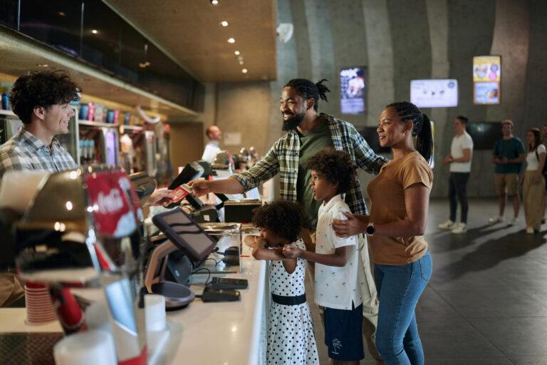 Des parents afro-américains heureux et leurs enfants achètent des billets au stand de la concession dans une arène sportive.